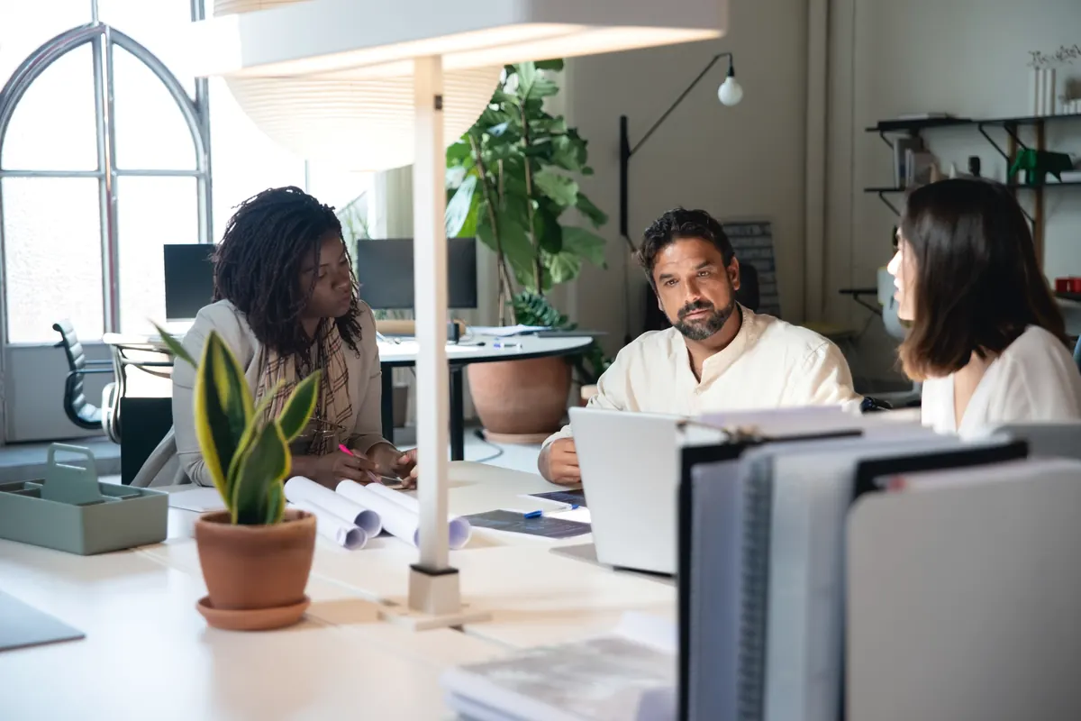 Trois collègues qui échangent autour d'un bureau, dans un open space lumineux